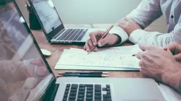 person holding pencil near laptop computer