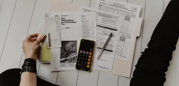 person holding paper near pen and calculator
